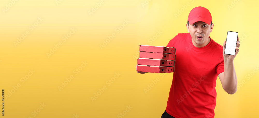 handsome Asian man in red cap, giving food order italian pizza in cardboard boxes isolated on yellow background in studio With copy space. holding mobile phone with blank white empty screen. handsome Asian man in red cap, giving food order italian pizza in cardboard boxes isolated on yellow background in studio With copy space. holding mobile phone with blank white empty screen.