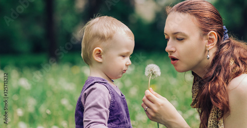 young mother and little daughter play with dandelion