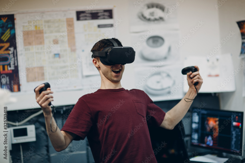 Young man in virtual reality goggles, vr glasses headset with joystick enjoying victory Young man in virtual reality goggles, vr glasses headset with joystick enjoying victory