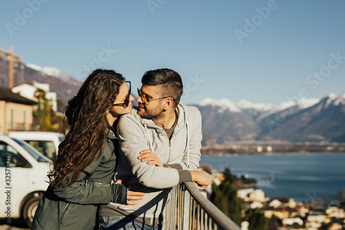 Beautiful couple in stylish clothes with glasses walking on snowy mountain background. Lovely couple travelling together in the Switzerland and walking around the lake Lugano. © eduard