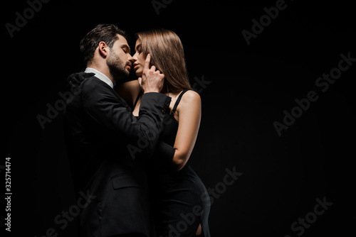 side view of handsome man touching face of attractive woman in dress isolated on black photo