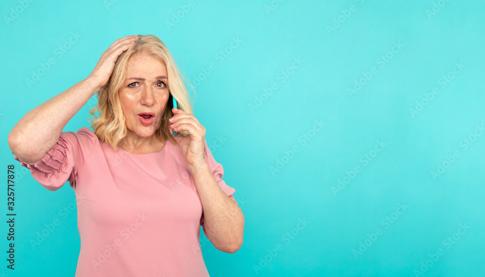 Surprised mid age woman standing in the blue studio and talking phone Surprised mid age woman standing in the blue studio and talking phone