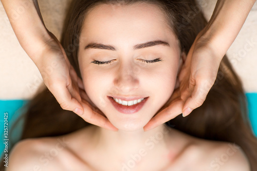 Young beautiful smiling woman receiving head face massage in beauty spa
