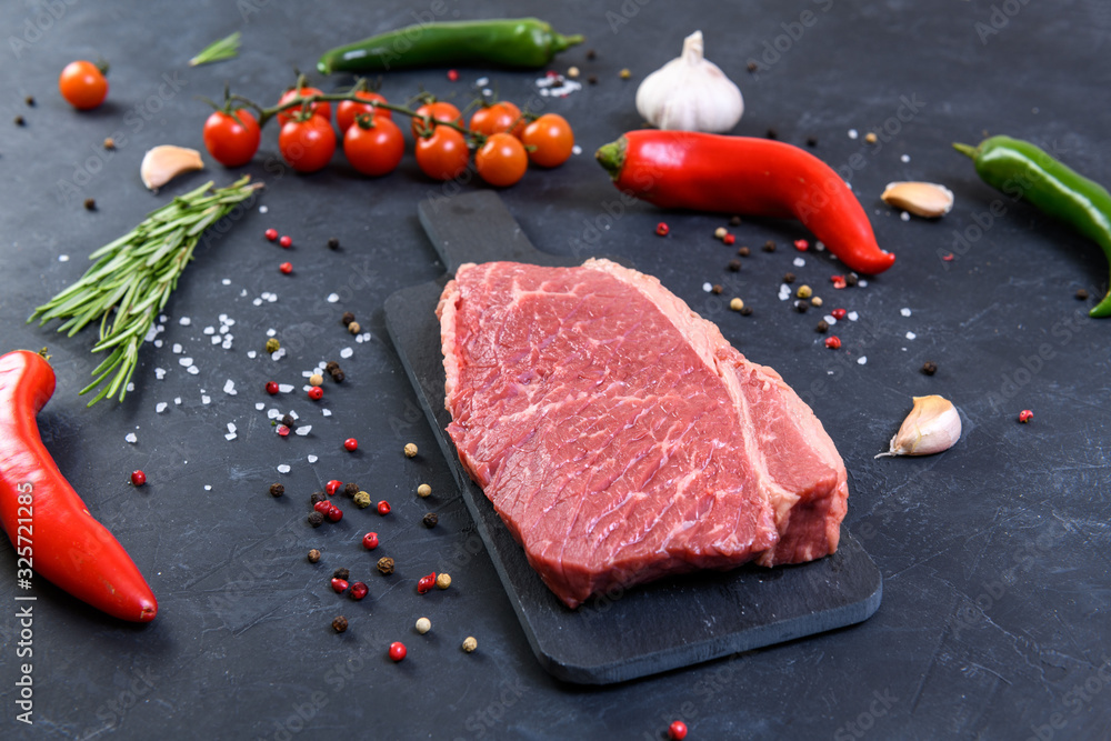 Raw fresh marbled meat and seasonings on dark background Raw fresh marbled meat and seasonings on dark background