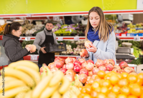 Portrait of positive woman buying ripe pomegranates in food store