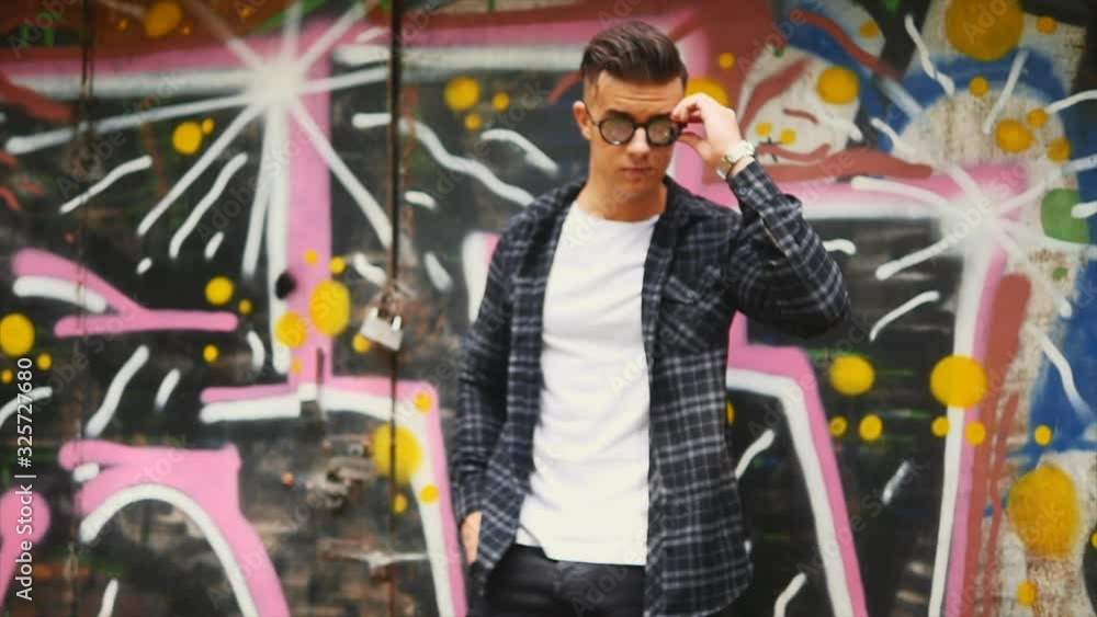 Confident guy is dressed in casual clothes, checked shirt. He is holding sunglasses with a pafos facial expression. Copy space. 4K. Confident guy is dressed in casual clothes, checked shirt. He is holding sunglasses with a pafos facial expression. Copy space. 4K.