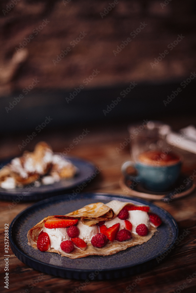Shrove Tuesday, Pancake Day. Delicious pancakes served with fresh strawberries, vanilla ice cream and icing sugar. Cup of coffee in the background. Concept of English traditions and food.