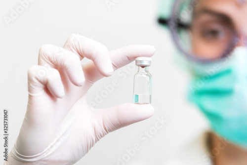 A doctor in medical gloves and mask holding an ampula with vaccine. Close up shot. Coronavirus, epidemic and medicine concept .