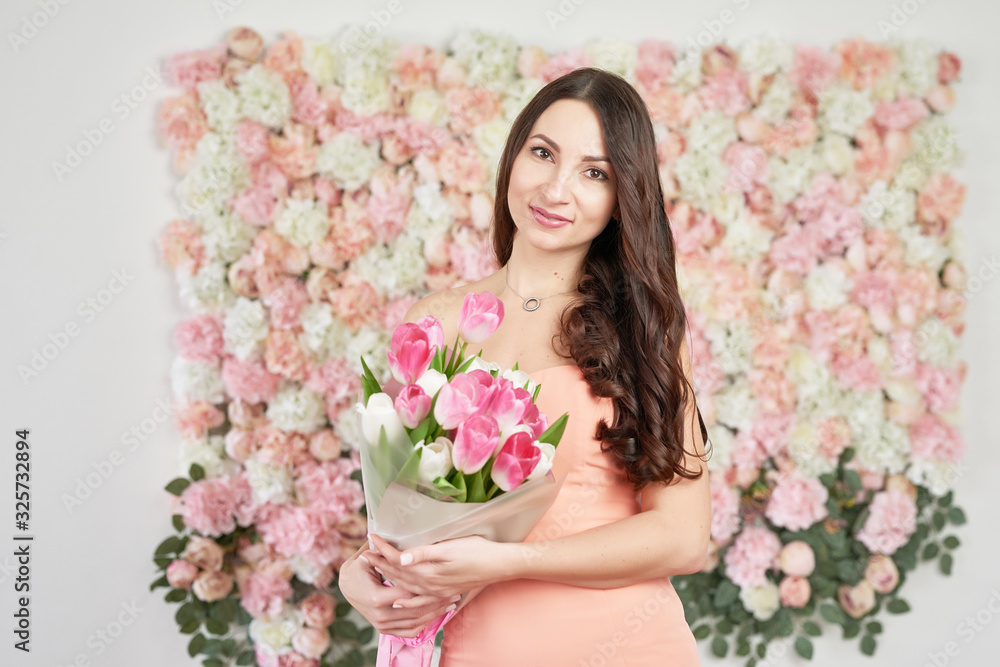 Beautiful girl with tulip flowers in hands on floral background. Greeting card for Women's Day March 8 or Mother's Day.Very nice florist woman holding beautiful colourful blossoming flowers bouquet