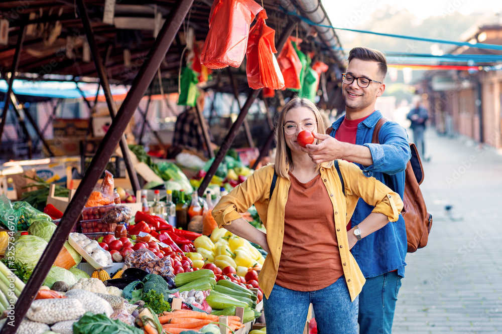 Beautiful young couple having fun buying fresh vegetables on outdoor market.