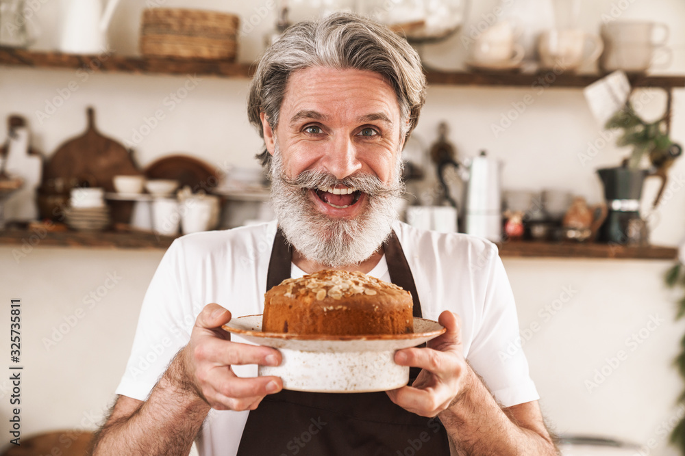 Image of excited mature man in apron smiling and showing cake Image of excited mature man in apron smiling and showing cake