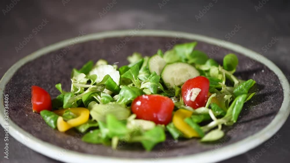 Woman adding salt in vegetable salad with greens, cucumbers, tomatoes, pepper. Mixing green salad falling on stone plate. Top view. Vegan and raw food concept. Woman adding salt in vegetable salad with greens, cucumbers, tomatoes, pepper. Mixing green salad falling on stone plate. Top view. Vegan and raw food concept.
