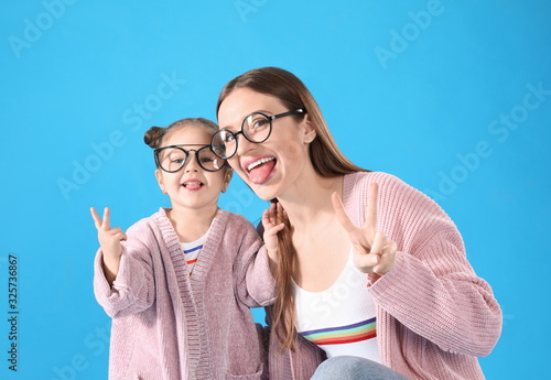 Young mother and little daughter with glasses on blue background