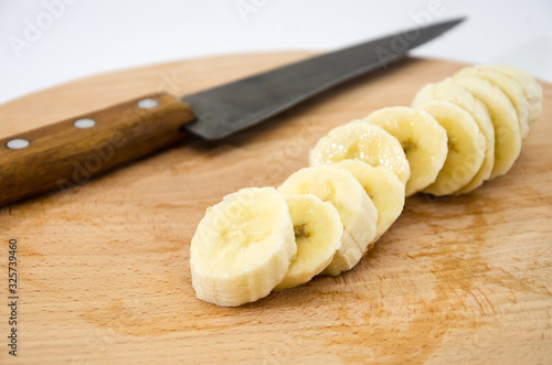 banana slices and knife on a wooden board on a white background. Close-up.