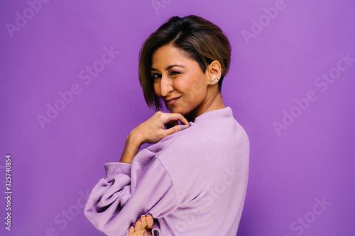 Portrait of young woman with her back to camera and short hair in the studio, with a purple background
