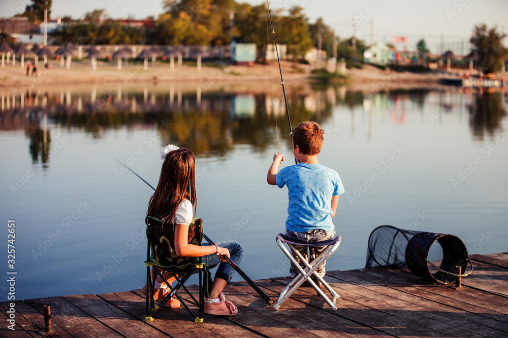 Two young cute little friends, boy and girl fishing on a lake in a sunny summer day Two young cute little friends, boy and girl fishing on a lake in a sunny summer day