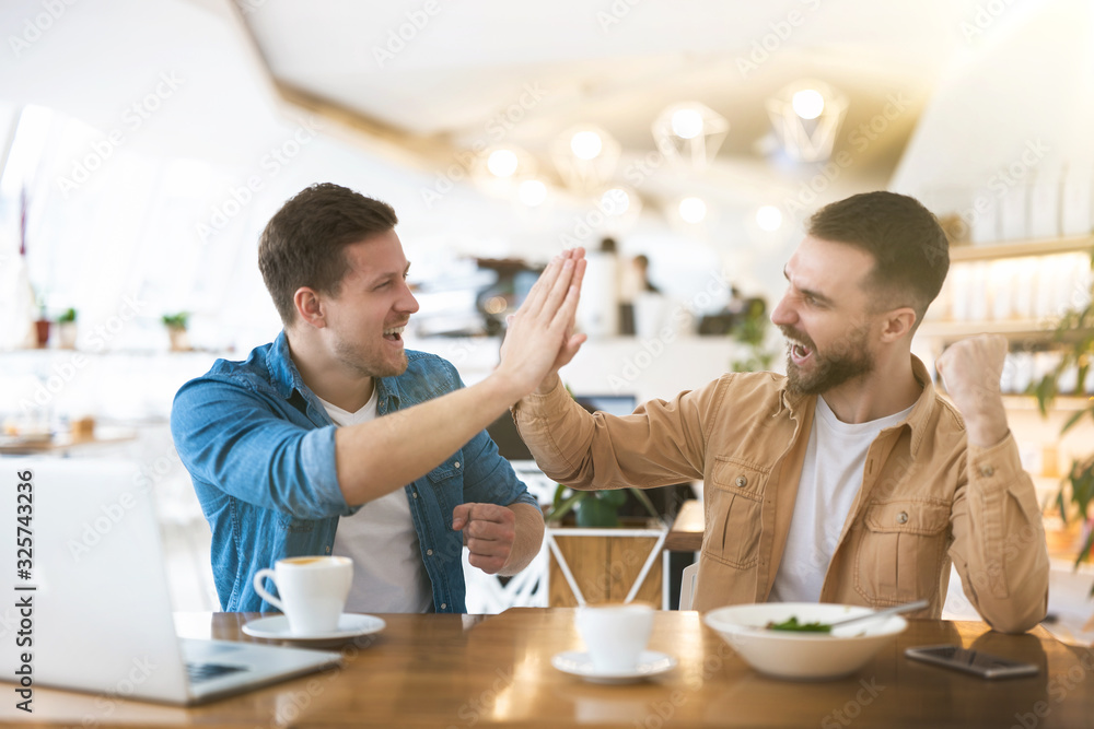 two colleagues men giving each other high five looking winning working on successful common project during lunch break at cafe, multitasking and teamwork concept two colleagues men giving each other high five looking winning working on successful common project during lunch break at cafe, multitasking and teamwork concept