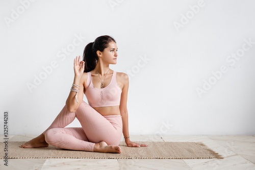 Positive caucasian young brunette woman doing Half lord of the fishes exercise, Ardha Matsyendrasana pose doing yoga. Yoga teacher woman doing gomukhasana on white background. Advertising space photo