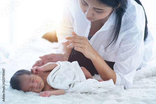 Young mother holding her newborn child on a white bed, mom and baby boy relaxing at home. maternity and child concept