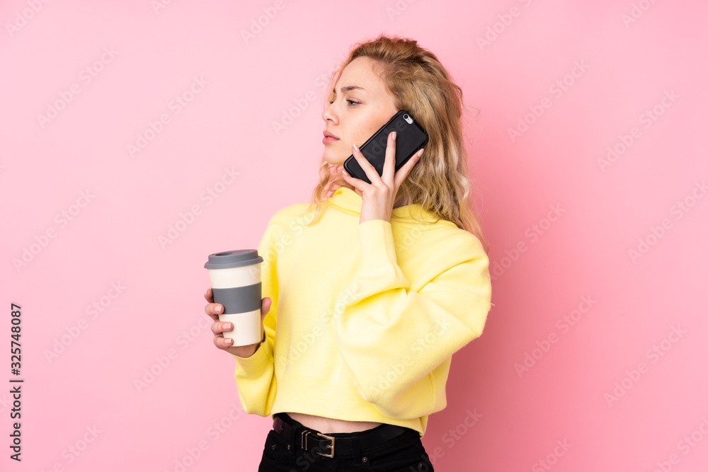Obraz premium Young blonde woman wearing a sweatshirt isolated on pink background holding coffee to take away and a mobile
