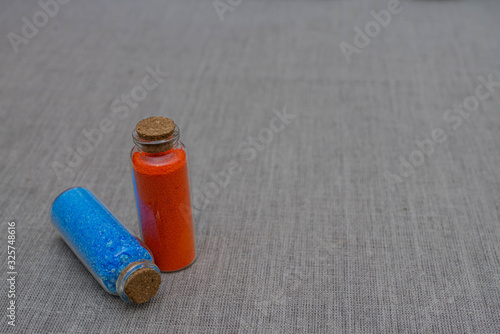 Blue and red powder and crystalls crystals in small bottles on gray linen background