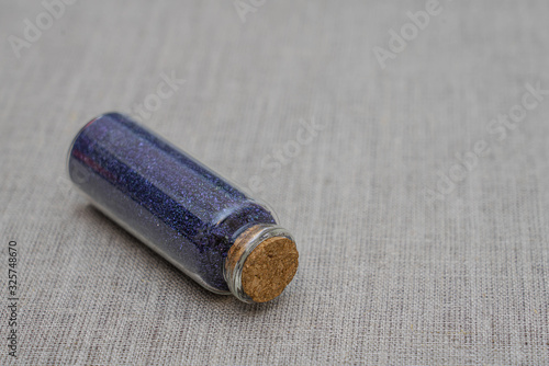 Blue powder and crystalls crystals in small bottle on gray linen background