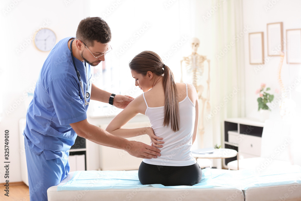Male orthopedist examining patient's back in clinic Male orthopedist examining patient's back in clinic