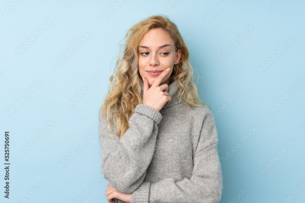 Young blonde woman wearing a sweater isolated on blue background looking to the side Young blonde woman wearing a sweater isolated on blue background looking to the side