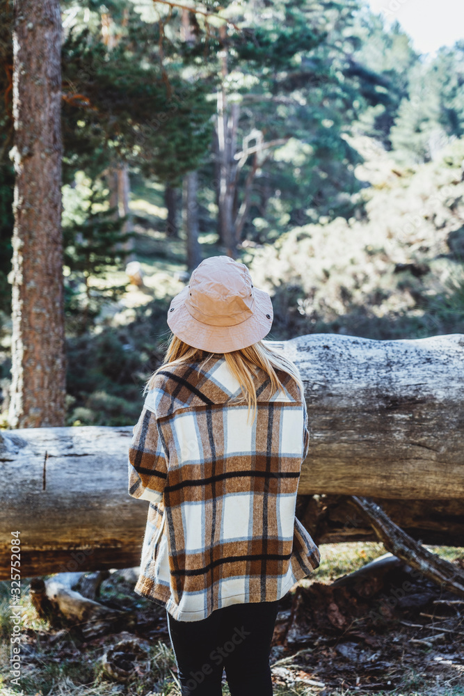 A blond woman with a hat and plaid shirt, sightseeing in a forest