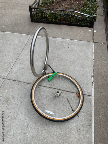 Stolen bicycle with remaining front tire locked to a bike rack. A single bicycle wheel on the street is all that is left due to stealing