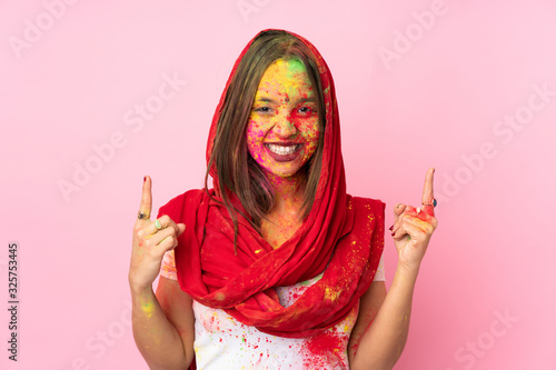 Young Indian woman with colorful holi powders on her face isolated on pink background pointing up a great idea