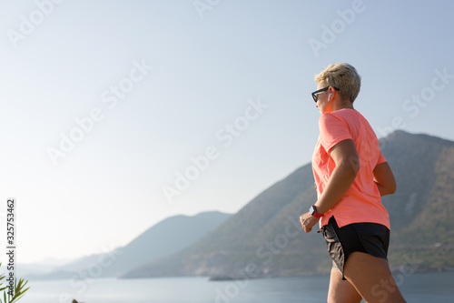 Female running in mountains under sunlight. Woman running on the mountain near the sea. Cross country runner