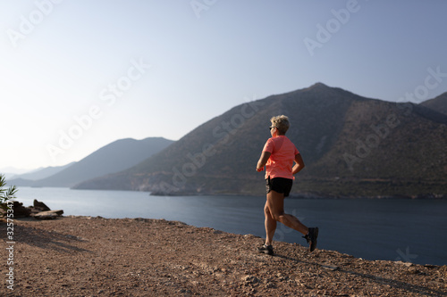 Female running in mountains under sunlight. Woman running on the mountain near the sea. Cross country runner © Irina