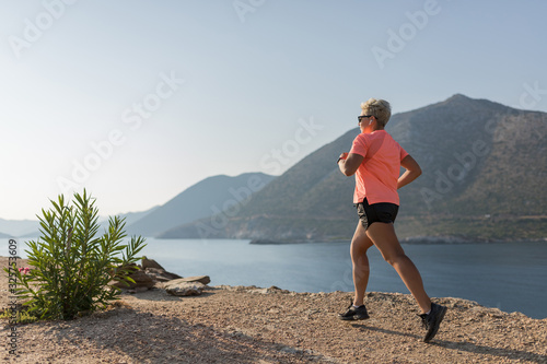 Female running in mountains under sunlight. Woman running on the mountain near the sea. Cross country runner