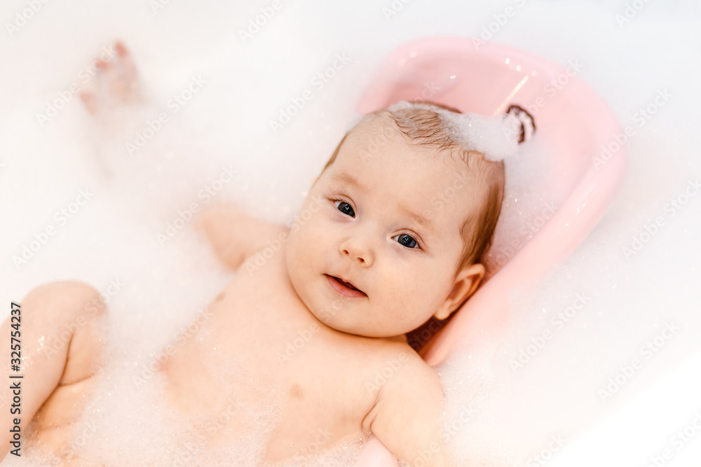 a small Caucasian baby is lying on a slide for bathing in foam a small Caucasian baby is lying on a slide for bathing in foam