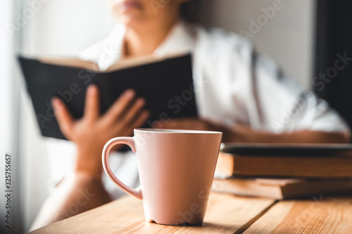 Woman in the morning drinks coffee and reads old book in a white shirt. Education, drink. manicure