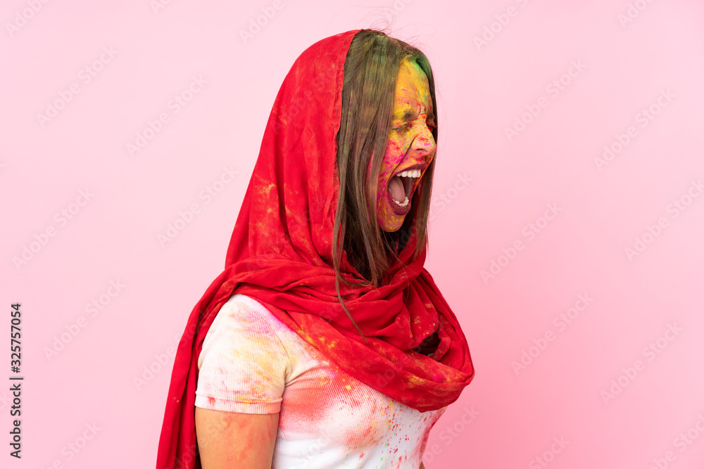 Fototapeta Young Indian woman with colorful holi powders on her face isolated on pink background laughing in lateral position
