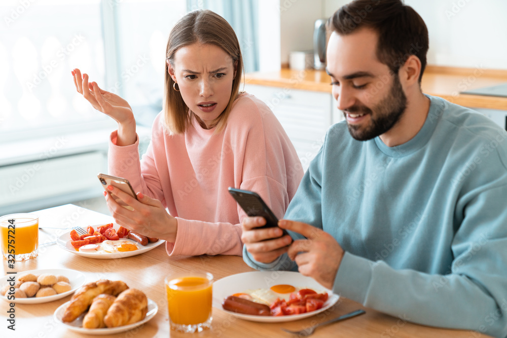 Portrait of young couple using cellphones while having breakfast Portrait of young couple using cellphones while having breakfast