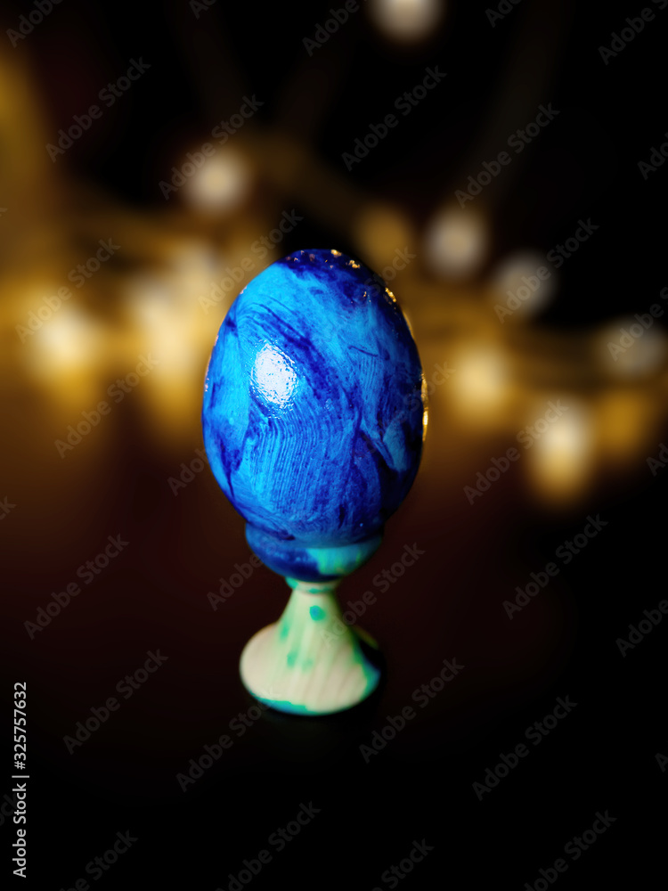 blue painted Easter egg on a black background with orange bokeh