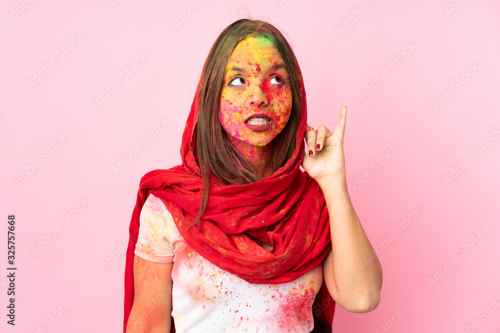 Young Indian woman with colorful holi powders on her face isolated on pink background listening to something by putting hand on the ear Young Indian woman with colorful holi powders on her face isolated on pink background listening to something by putting hand on the ear