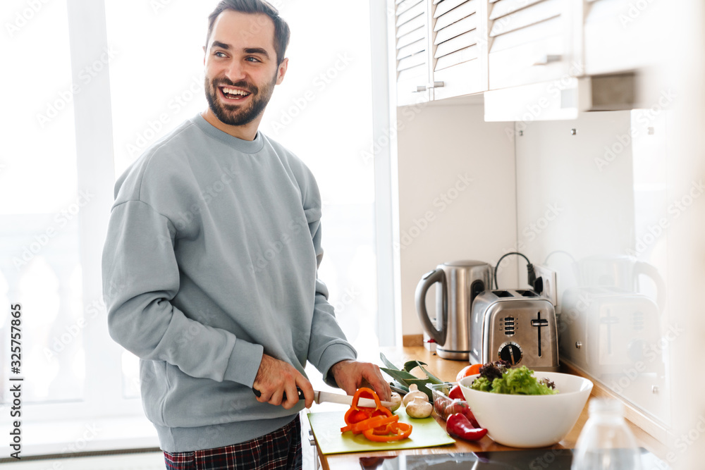 Image of pleased handsome man smiling and making lunch Image of pleased handsome man smiling and making lunch