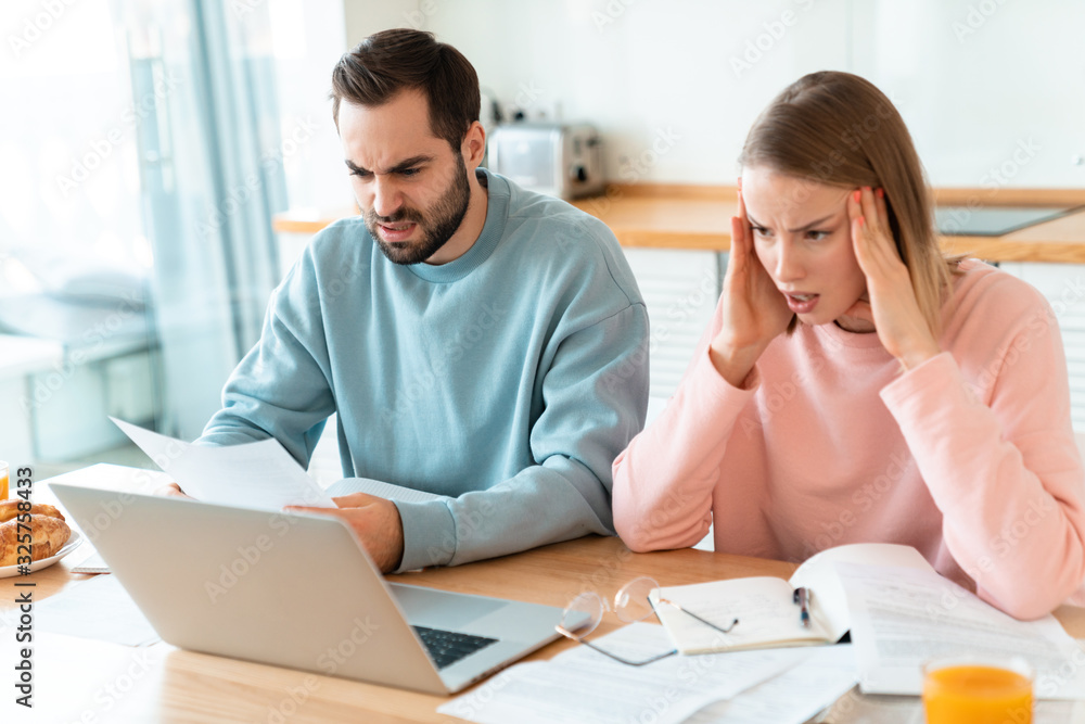 Portrait of young brooding couple working with laptop and documents