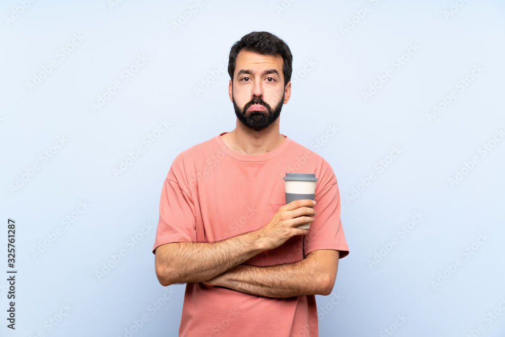 Young man with beard holding a take away coffee over isolated blue background with sad and depressed expression Young man with beard holding a take away coffee over isolated blue background with sad and depressed expression