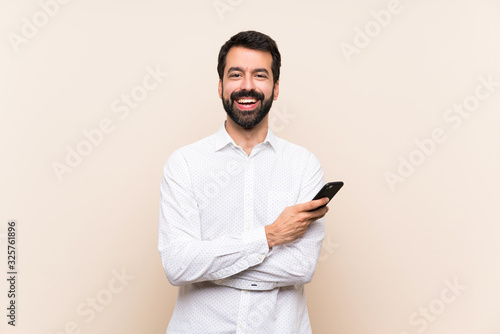 Young man with beard holding a mobile keeping the arms crossed in frontal position