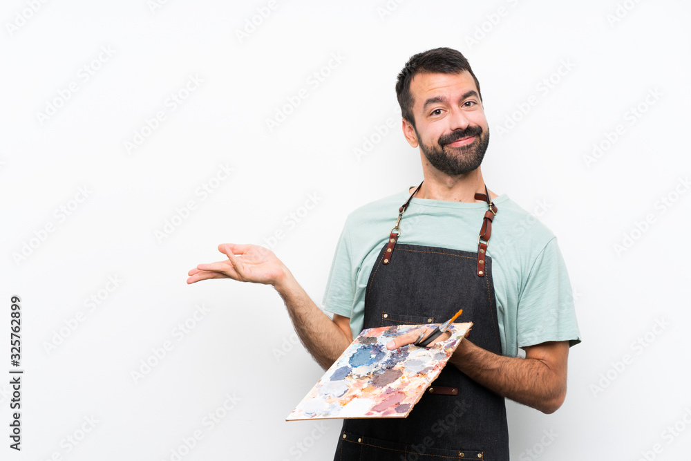 Young artist man holding a palette over isolated background extending hands to the side for inviting to come Young artist man holding a palette over isolated background extending hands to the side for inviting to come