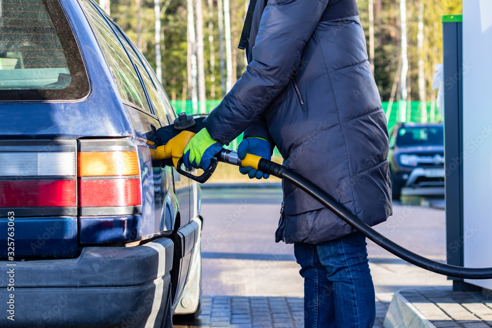 girl in a warm jacket refuel the car in yellow gloves. Close-up. girl in a warm jacket refuel the car in yellow gloves. Close-up.