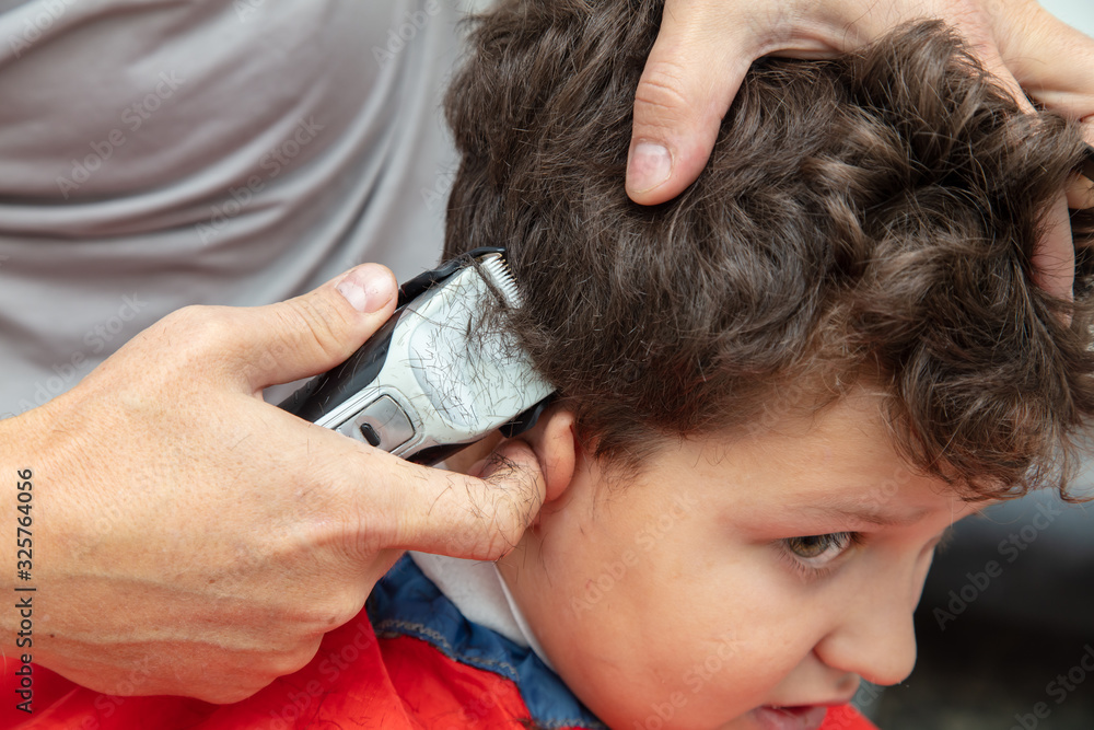 Naklejka premium The hairdresser cuts the hair of a boy with a machine