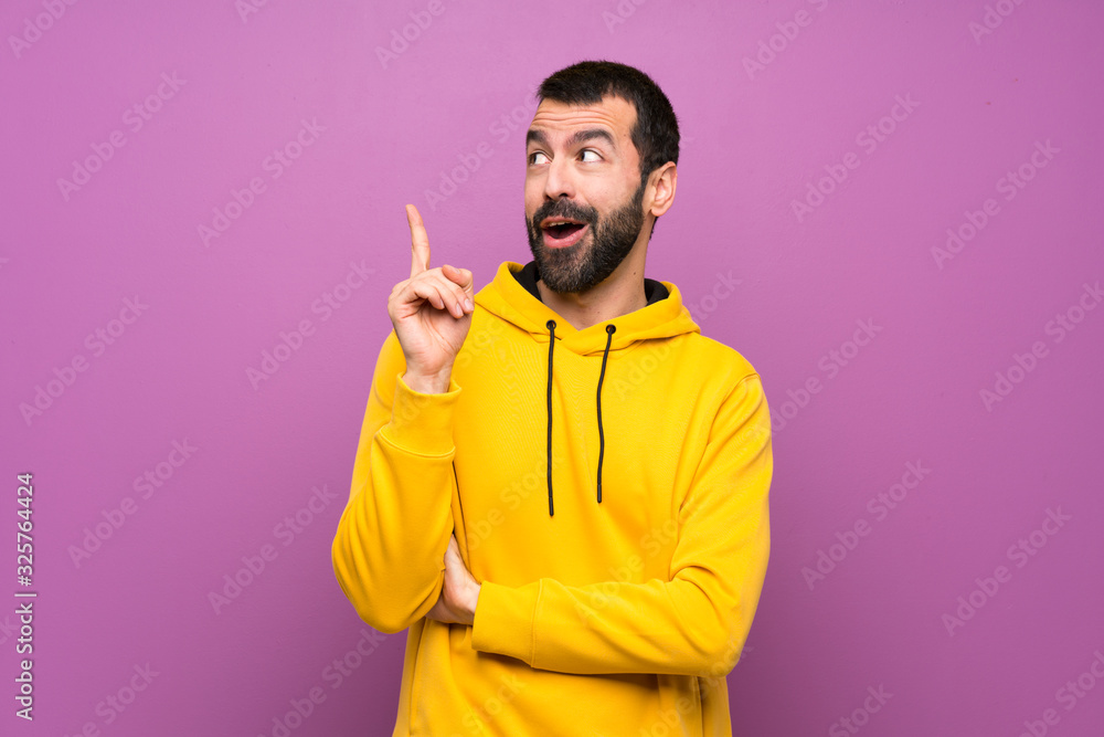 Handsome man with yellow sweatshirt intending to realizes the solution while lifting a finger up Handsome man with yellow sweatshirt intending to realizes the solution while lifting a finger up