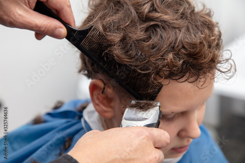 The hairdresser cuts the hair of a boy with a machine