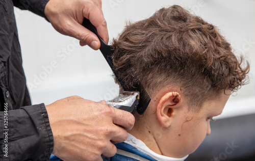 The hairdresser cuts the hair of a boy with a machine